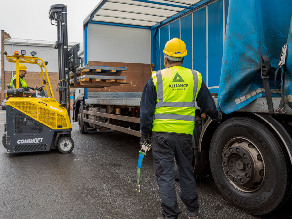 Two men with hardhats and high vests on loading goods to be transported